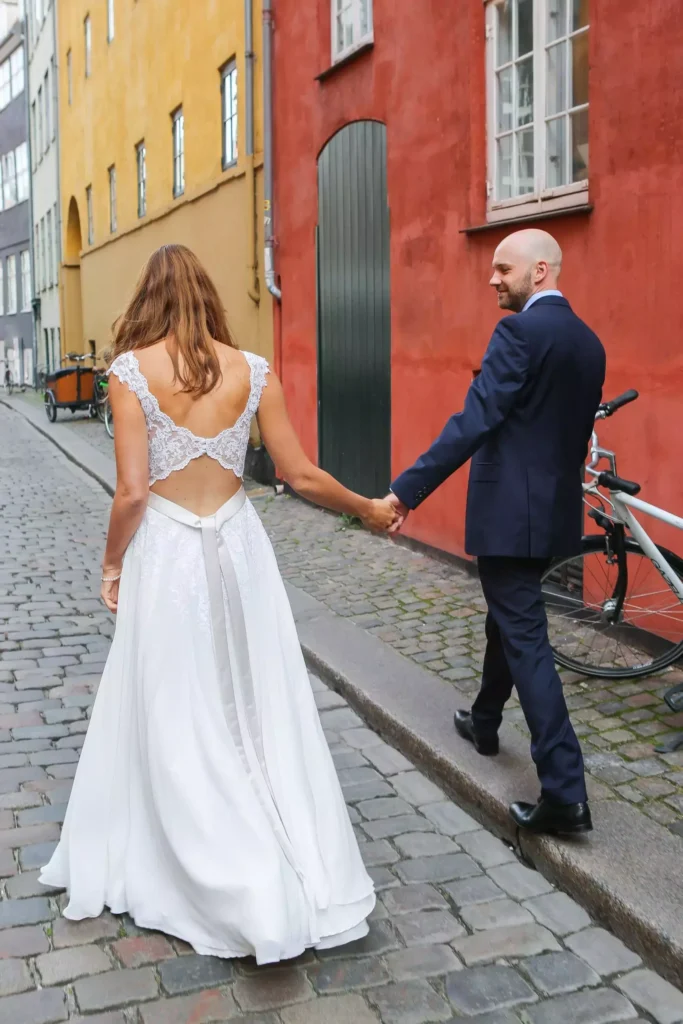 Frisch verheiratetes Paar geht Hand in Hand durch die Straßen von Kopenhagen mit bunten Gebäuden im Hintergrund.