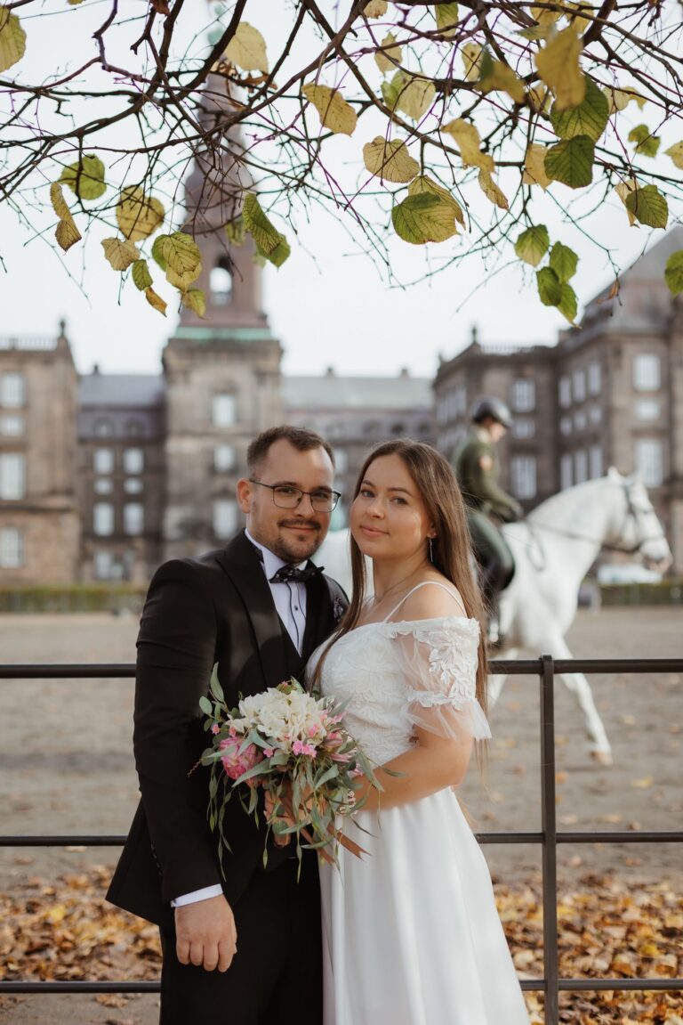 Heiraten in Denemarken: Een paar Brauts stellen zich op voor Christiansborg Slot met een Reiter op een witte Pferd in de achtergrond.