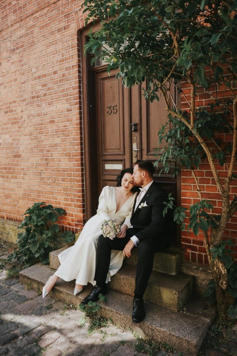 Heiraten in Denemarken: Hochzeitspaar sitzt romantisch voor een andere Holztür mit Ziegelwand.