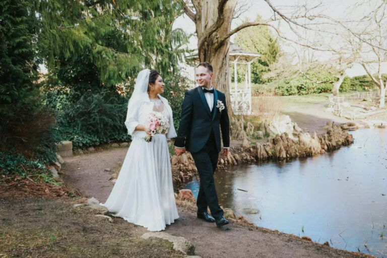 Ein Hochzeitspaar spaziert glücklich durch einen malerischen Park neben einem ruhigen Teich.