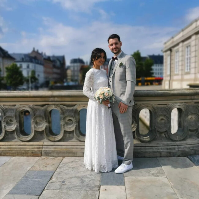 Hochzeitspaar in Kopenhagen auf einer historischen Brücke mit urbanem Hintergrund und klarem Himmel.