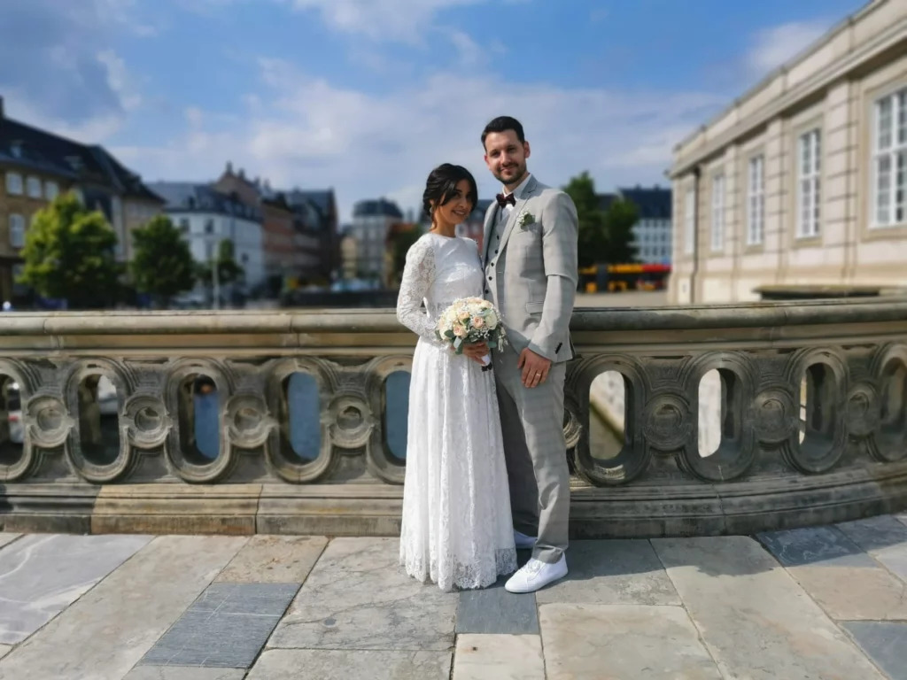 Hochzeitspaar in Kopenhagen auf einer historischen Brücke mit urbanem Hintergrund und klarem Himmel.