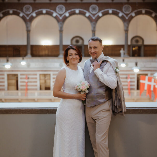 Hochzeit in Dänemark – Get married in Denmark mit einzigartigem Charme und Tradition Heiraten in Dänemark: Ein elegantes Brautpaar posiert nach der standesamtlichen Trauung in einem historischen Gebäude mit dänischen Flaggen.