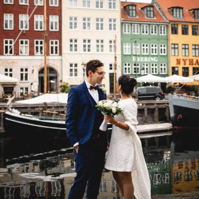 Hochzeitspaar in Nyhavn, Kopenhagen, vor bunten Häusern und einem Kanal mit Segelbooten.